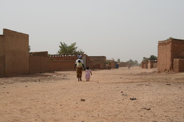 A mother with her two daughters, one on her back and the other holding her hand, walking down a road in Rimkieta